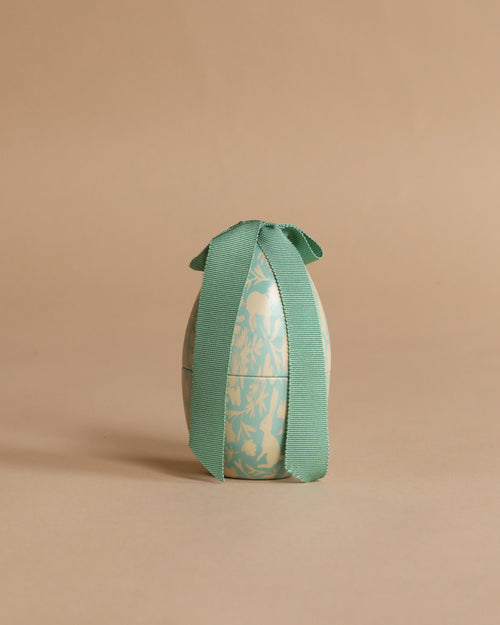 The Maileg Easter Egg, Small - Dusty Mint, featuring a delicate floral pattern and a wide green bow, stands upright on a simple beige background.