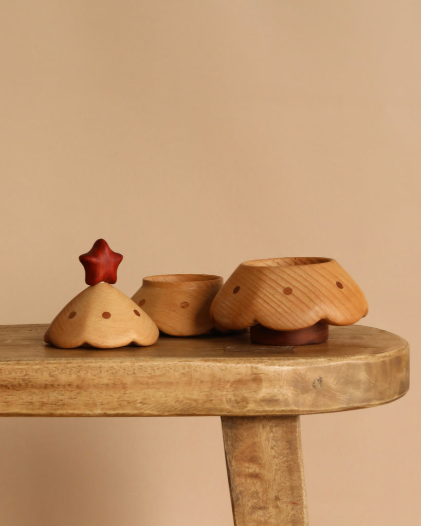 Three small, light wooden Christmas Tree Storage Boxes with scalloped edges and polka dot accents sit on a rustic wooden surface. One features a red, star-shaped handle, perfect for festive storage. The background is solid beige.