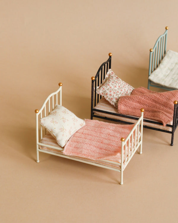 Two Maileg Miniature Beds with detailed frames, pillows, and textured bedspreads in shades of white and pink, arranged on a soft beige background.