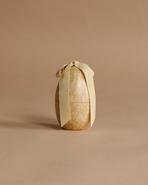 The Maileg Easter Egg, Small - Cream Yellow features a subtle floral pattern and a cream-colored ribbon bow. Crafted from metal, this charming decorative egg adds an elegant touch to your spring or Easter celebrations.