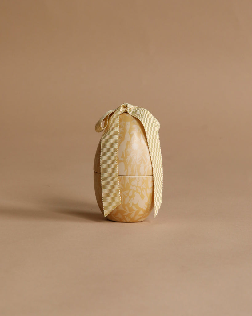 The Maileg Easter Egg, Small - Cream Yellow features a subtle floral pattern and a cream-colored ribbon bow. Crafted from metal, this charming decorative egg adds an elegant touch to your spring or Easter celebrations.