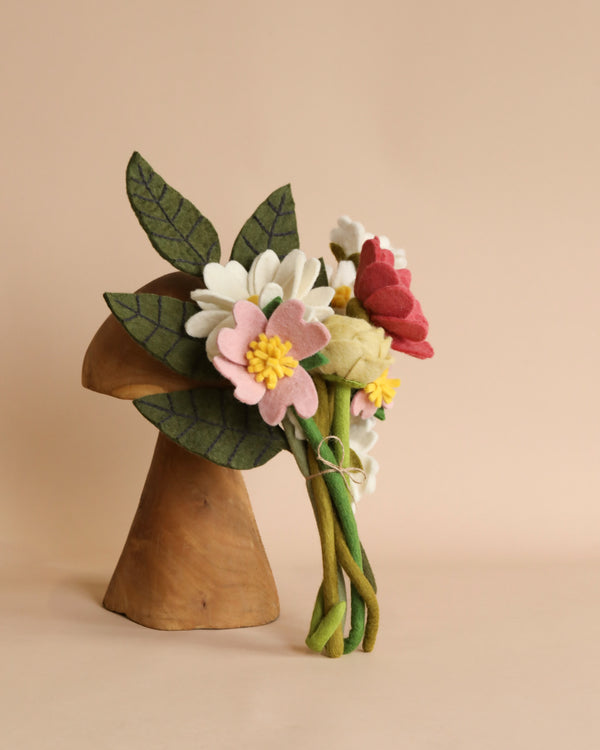 A wooden head-shaped vase displaying a Felt Flower Bouquet - Blossom, artistically arranged against a soft beige background.
