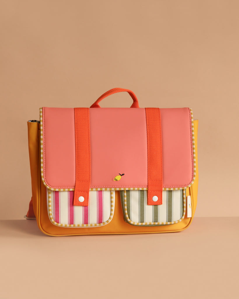 The Sticky Lemon School Bag in Coral Pink and Submarine Yellow, made of waterproof nylon, features a colorful design with an orange body, pink flap, red straps, and striped front pockets against a beige background.