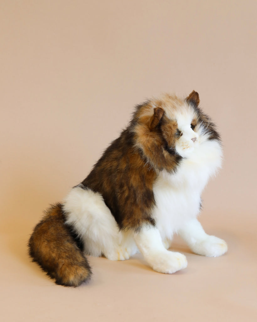 A fluffy calico Forest Cat Stuffed Animal with a thick white, black, and brown coat, sitting gracefully against a light beige background, looking to the side.