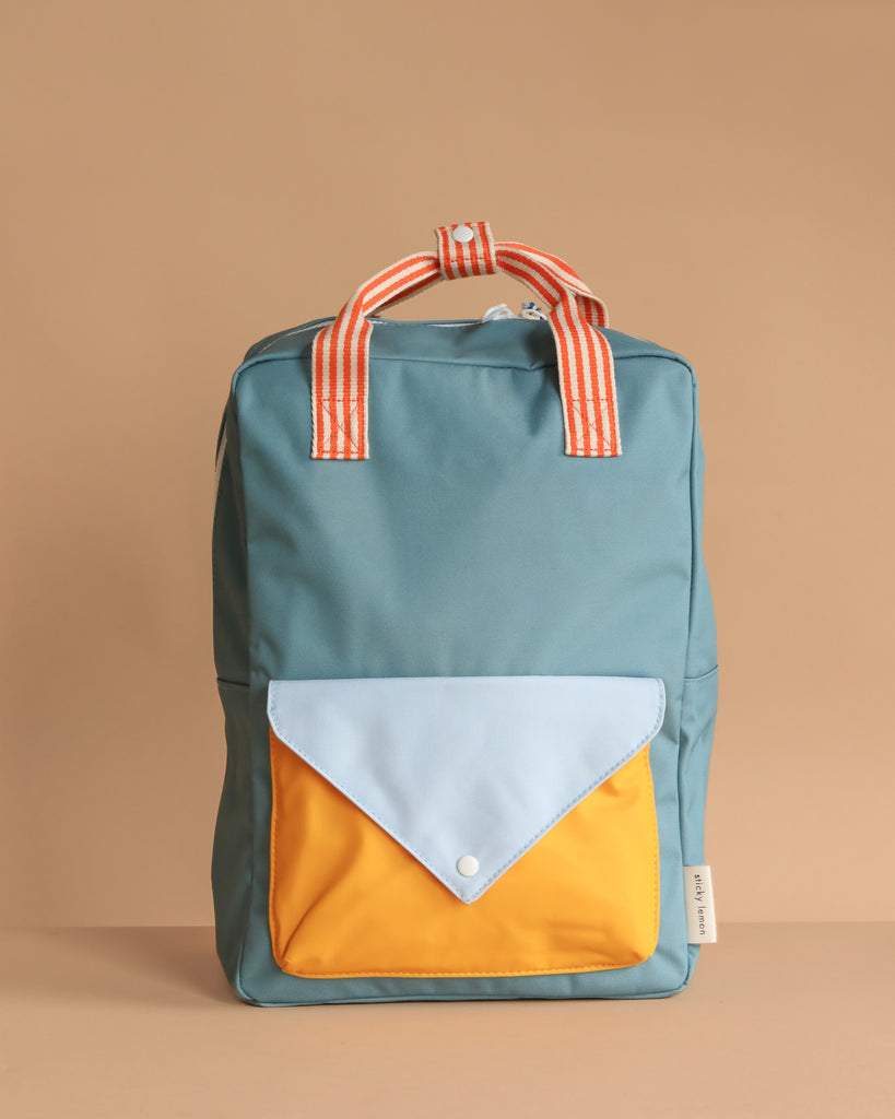 The Sticky Lemon Backpack Large | Envelope | Diving Suit features a teal color, orange-and-white striped handles, a front pocket with a blue flap and yellow body, made from recycled PET bottles and shown against a plain beige background.