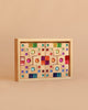 The Bauspiel Colored Staircase with Luminous Blocks - 32 Piece is a light brown rectangular wooden box featuring a vibrant, symmetrical front display of gem-like circles, squares, and rectangles—perfect for lovers of unique wooden construction sets.