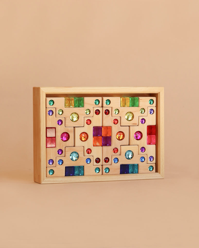 The Bauspiel Colored Staircase with Luminous Blocks - 32 Piece is a light brown rectangular wooden box featuring a vibrant, symmetrical front display of gem-like circles, squares, and rectangles—perfect for lovers of unique wooden construction sets.
