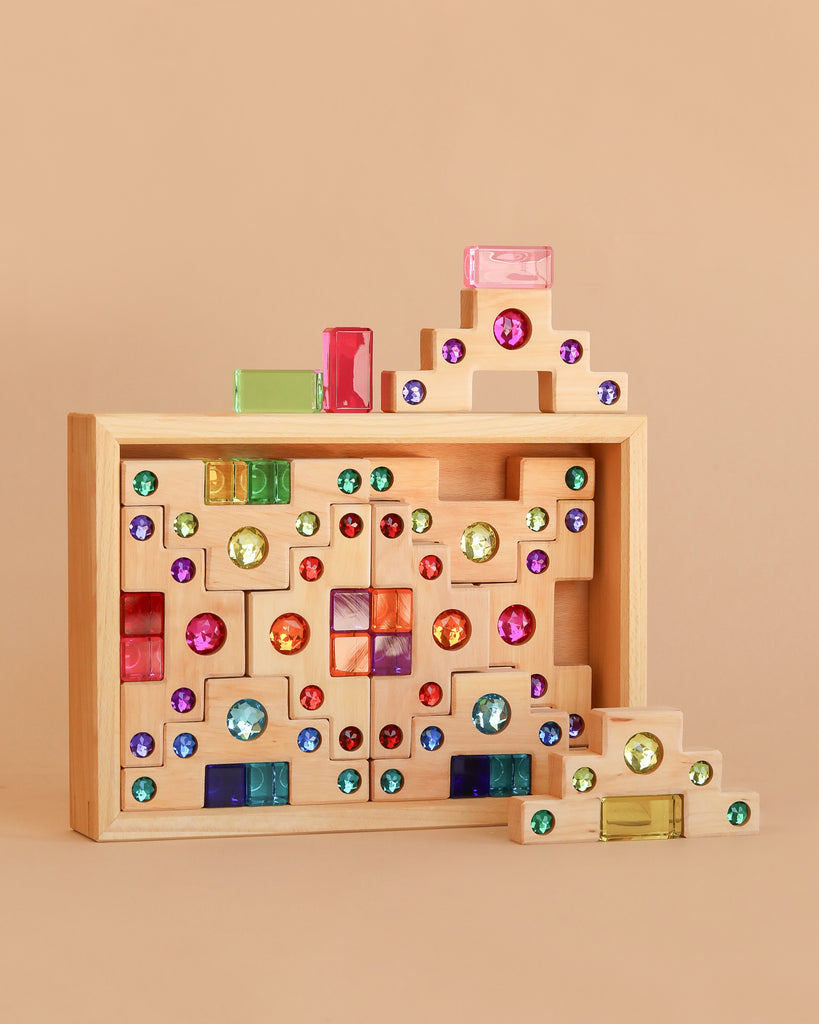 The Bauspiel Colored Staircase with Luminous Blocks - 32 Piece features colorful, translucent building blocks arranged in geometric patterns, with some luminous pieces stacked outside the box on a neutral background.