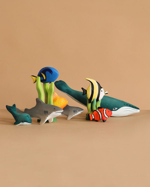 The Bumbu Handmade Wooden Under the Sea Set features colorful, handcrafted wooden ocean animals—whale, sharks, clownfish, and tropical fish—arranged on a beige background, ideal for Waldorf-inspired or Montessori play.