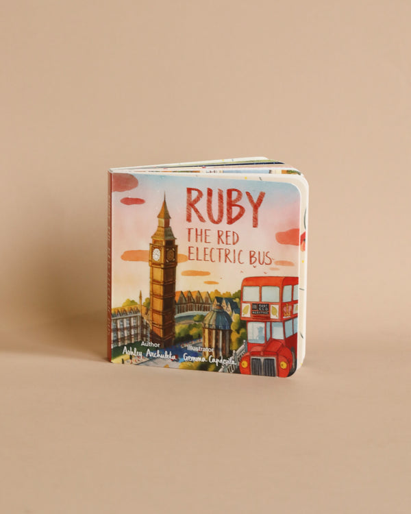 A colorful children's Ruby The Red Electric Bus Book with illustrations of London landmarks and a red double-decker bus on the cover, placed against a plain beige background.
