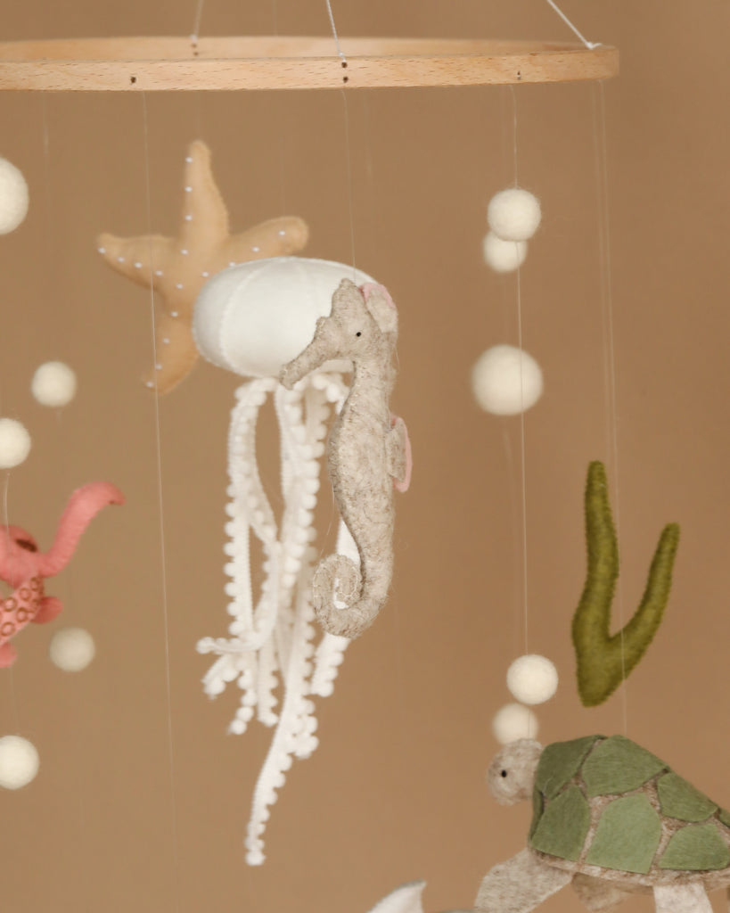 A whimsical Handmade Mobile - On The Reef - Final Sale featuring various marine-themed felt figures, including a seahorse, jellyfish, starfish, turtle, and octopus. Handmade in Europe, the figures are suspended by strings from a wooden hoop, creating a playful and soothing oceanic scene perfect for nursery decoration and visual development.