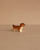 The Handmade Holzwald Dachshund Dog, Small, is a charming brown and white wooden figurine displayed on a beige surface—perfect for lovers of sustainable and classic wooden toys.