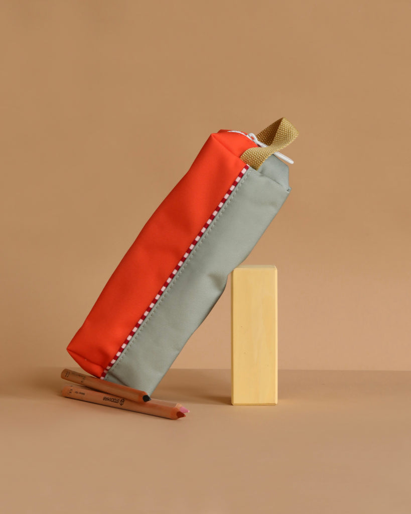 The Sticky Lemon Pencil Case | Color Blocking | Lifebuoy Orange + Shark Grey, made from recycled PET bottles, stands upright next to two colored pencils on a beige background, highlighting its orange and gray color block design.