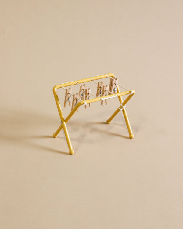 A small, yellow Maileg Drying Rack, Mouse Size with small wooden pegs attached to its bars is positioned against a plain beige background. The drying rack is empty, with no clothing or items hanging on it.