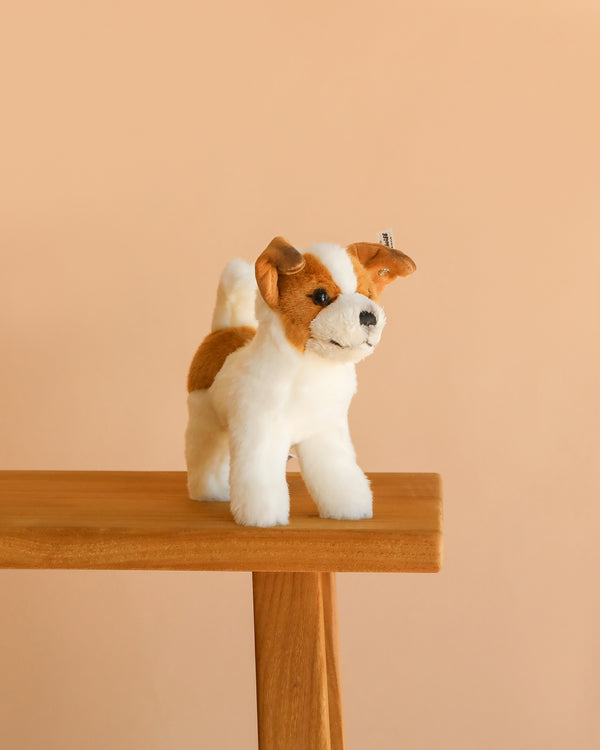 The Steiff Terrie Dog, a realistic stuffed dog with brown and white fur, stands on a light wooden table against a plain beige background.