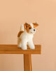 The Steiff Terrie Dog, a realistic stuffed dog with brown and white fur, stands on a light wooden table against a plain beige background.