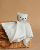 The Cuddle + Kind Organic Cotton Baby Bear Lovey (Baby Blue), a soft fair trade lovey with a knitted bear head and blanket body, is displayed over a woven wicker basket against a light brown background—perfect as a cozy baby gift.