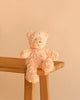 An 8" Steiff Baby Jimmy Teddy Bear, featuring soft, light peach plush fur, the classic Steiff Button in Ear, and a yellow tag, sits on the corner of a wooden bench against a beige background.