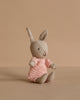 The Maileg Rabbit Micro - Sand wears a rose knitted suit and sits upright, featuring soft beige fur and long ears—ideal as a Maileg accessory or for a miniature dollhouse, photographed against a plain beige background.