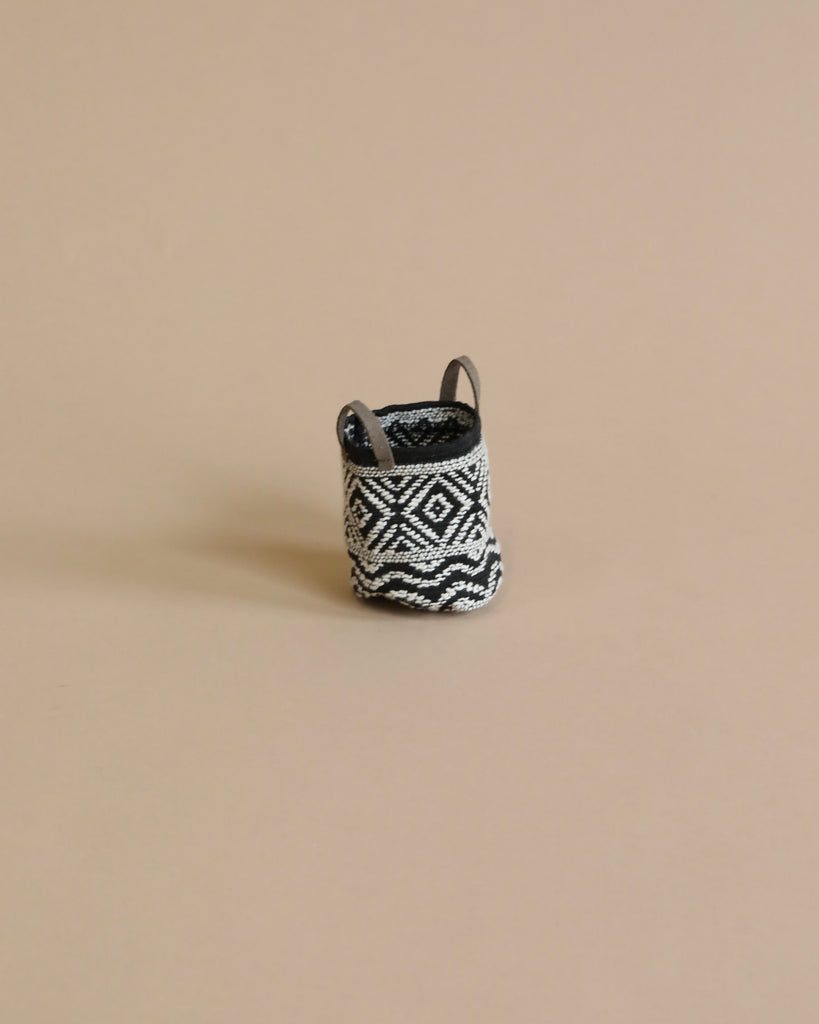A small, handcrafted Maileg | Miniature Basket with black and white geometric patterns, displayed against a plain beige background.