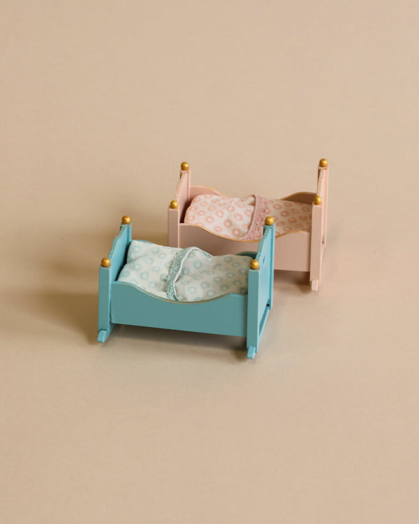 Two Maileg Miniature Cradles in blue and pink colors, each fitted with a patterned bedding set, against a neutral beige background.
