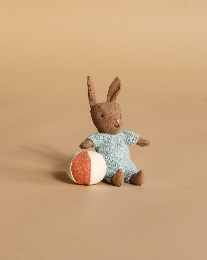 The Maileg Micro Bunny With Ball - Brown - Blue features a soft brown bunny in a blue outfit with magnetic hands, sitting beside a small white and orange ball—an adorable addition to any bunny collection.
