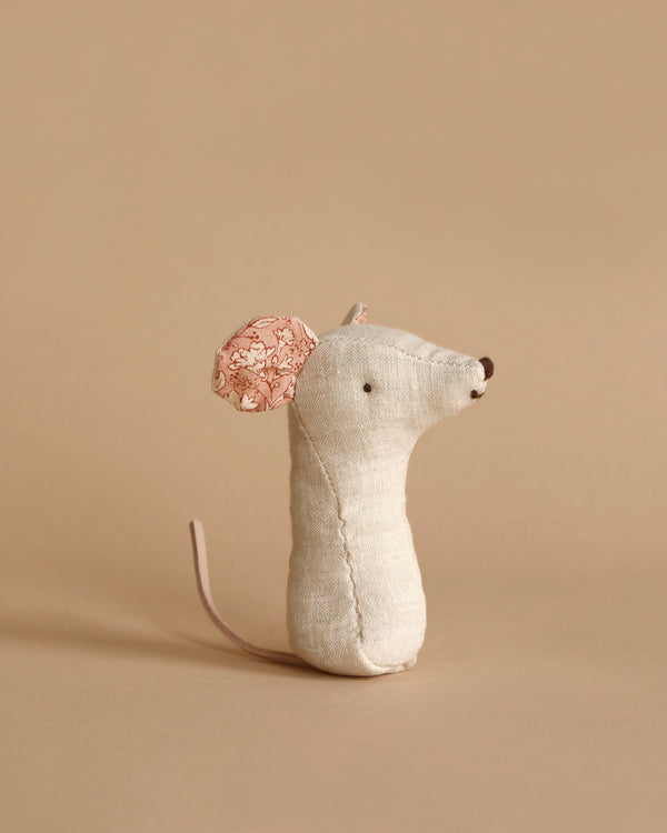 A small, stuffed fabric Maileg Lullaby Friend Rattles, Mouse - Nature on a plain beige background. The toy doubles as a soft baby rattle and has a simple design with minimal facial features, a long tail, and one ear with a pink floral pattern. The other ear is plain beige linen matching the body, making it an ideal gift box addition.