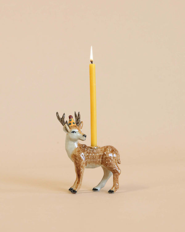 A decorative Stag Cake Topper with a yellow candle mounted on its back, set against a plain beige background. The candle is lit, adding a warm glow.