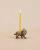 A whimsical, hand-painted Lion Cake Topper shaped like a lion with a lit yellow candle on its back, set against a soft beige background.