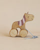 A Handmade Wooden Unicorn Pull Toy crafted from sustainably harvested birch wood, shaped like a smiling horse with purple details and a patterned ribbon on its ear, standing against a pale background.