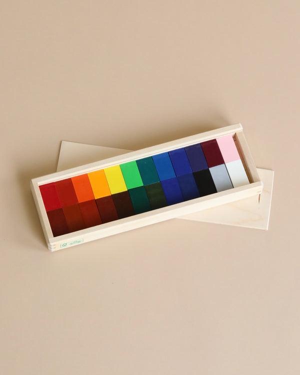 A color calibration card featuring a series of vibrant squares ranging from bright red to deep black, displayed in an open white case on a beige background with Stockmar Wax Block Crayons Wooden Box - 24 Assorted.