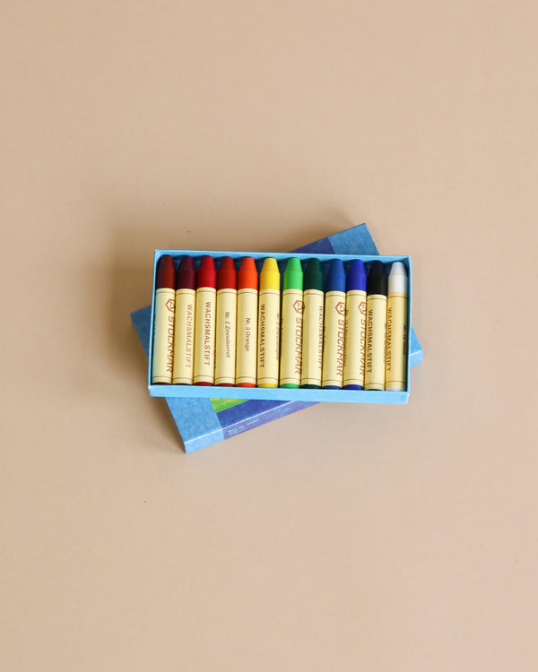 A box of Stockmar Wax Stick Crayons with various colors ranging from red to blue, neatly arranged and displayed on a light beige background.