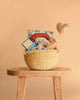 The Easter Basket Gift Set, displayed on a wooden stool against a peach background, includes plush toys, a children’s book, Maileg mice, a chocolate bar, and a gold glittery heart wand.