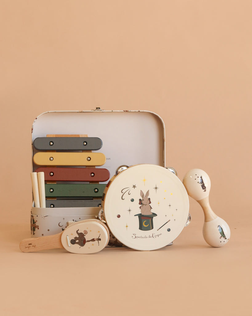 The Konges Sloejd Music Set - Circus, featuring a xylophone, tambourine, maracas, and castanet adorned with charming animal illustrations, is arranged in front of an open musical suitcase on a beige background.