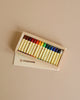 A box of Stockmar Wax Stick Crayons Wooden Box - 16 Assorted with various colors displayed in an open white cardboard box on a light beige background.