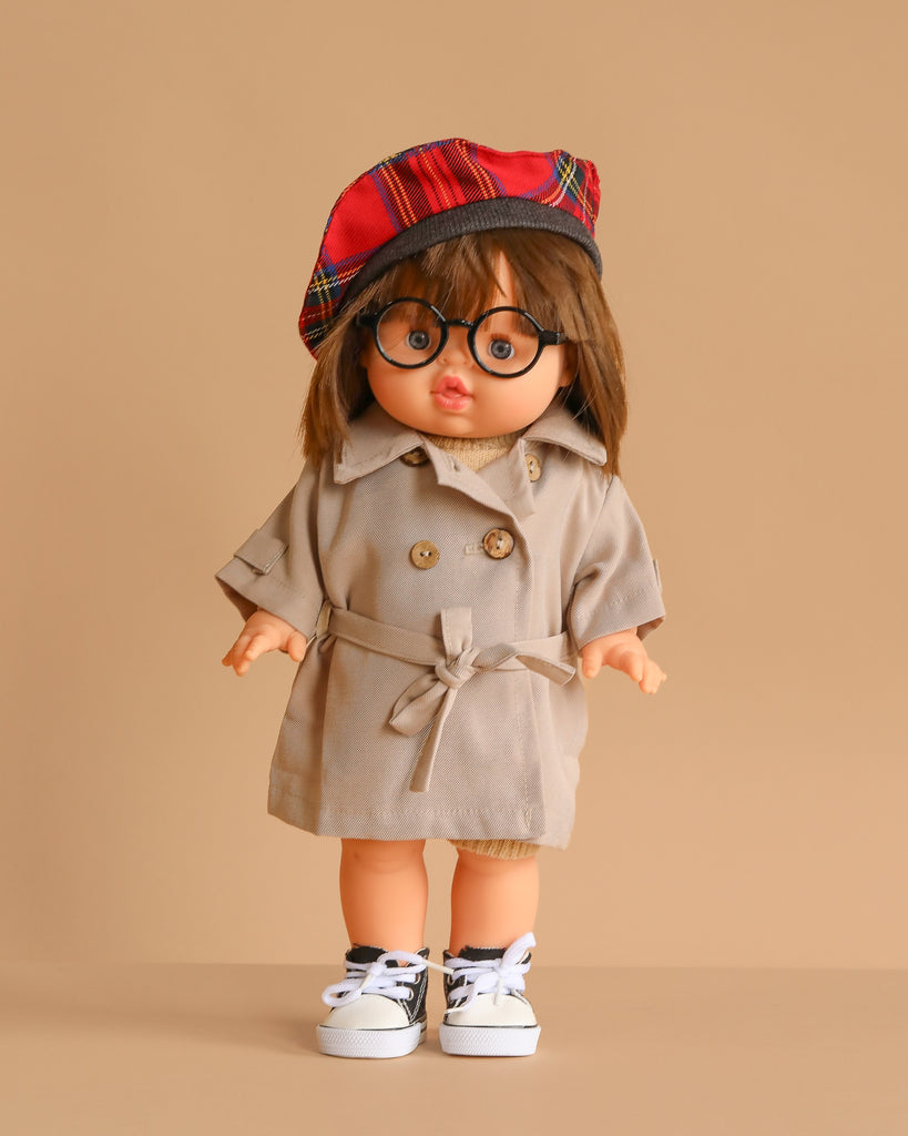 The Minikane Standing Doll (14") - Chléa With Clothing features brown hair, round glasses, and a red plaid beret, dressed in a beige trench coat and white sneakers. Stands against a beige background. Made in Spain.