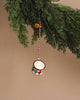 The Maileg Metal Ornament, Small Drum - Classic Red, features hand-painted details in a red and blue harlequin pattern and hangs from a red and white string on a fir branch. The neutral beige background enhances this festive decor, combining nostalgic charm with artisanal elegance.