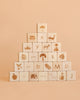 A pyramid of Sabo Concept Alphabet Wooden Blocks - Natural, crafted from natural linden wood and engraved with images and letters featuring animals, objects, and symbols, arranged on a beige background.