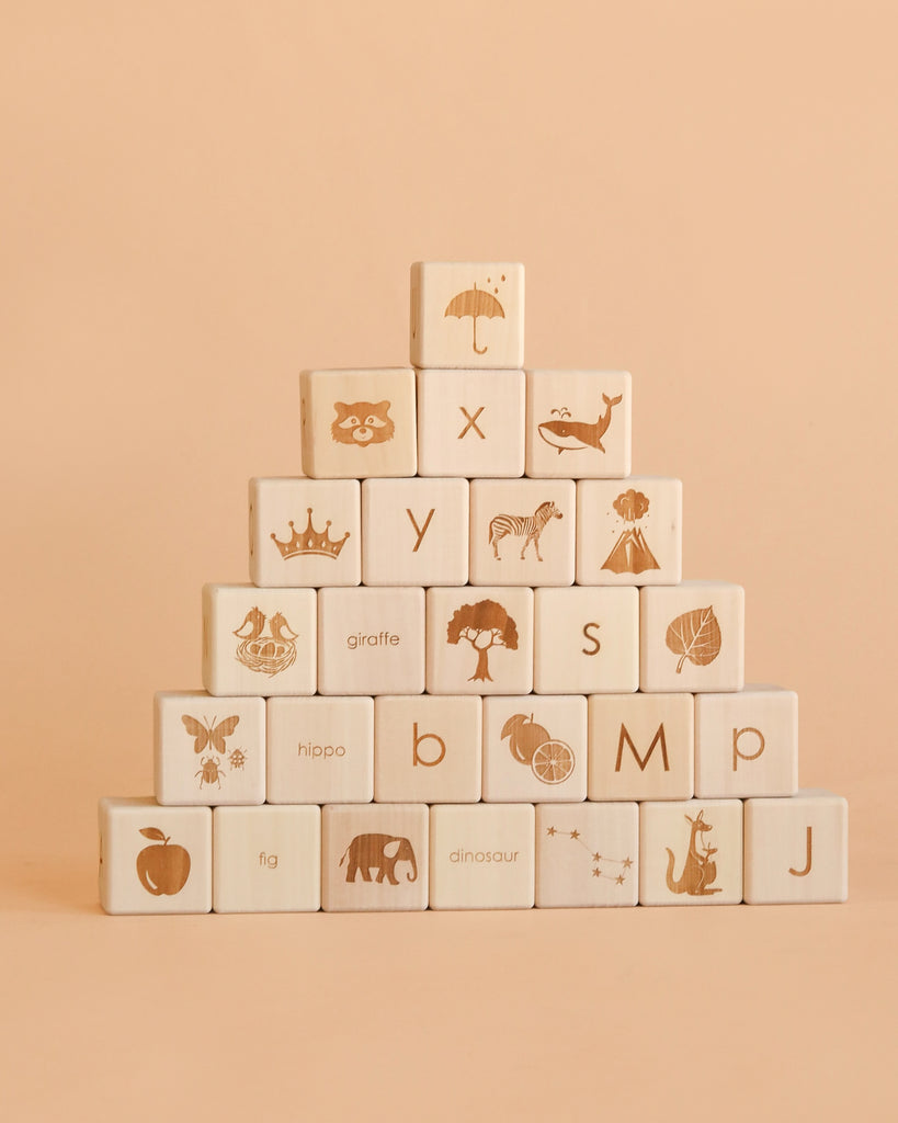 A pyramid of Sabo Concept Alphabet Wooden Blocks - Natural, crafted from natural linden wood and engraved with images and letters featuring animals, objects, and symbols, arranged on a beige background.