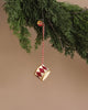 The Maileg Metal Ornament, Small Drum - Red hangs by a twine from a green pine branch against a beige background, showcasing handpainted details.