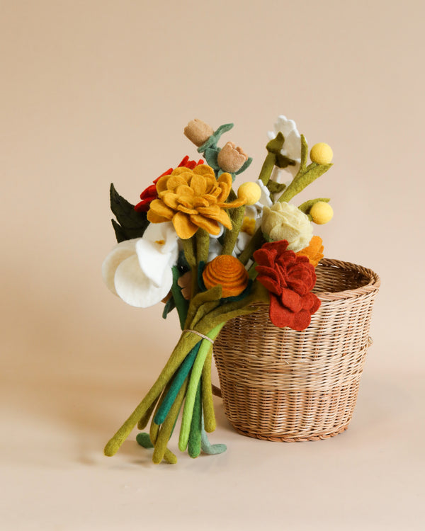 A delicate arrangement of eco-friendly, handcrafted Felt Flower Bouquet - Autumn in a wicker basket, showcasing various flowers in warm colors against a soft beige background.