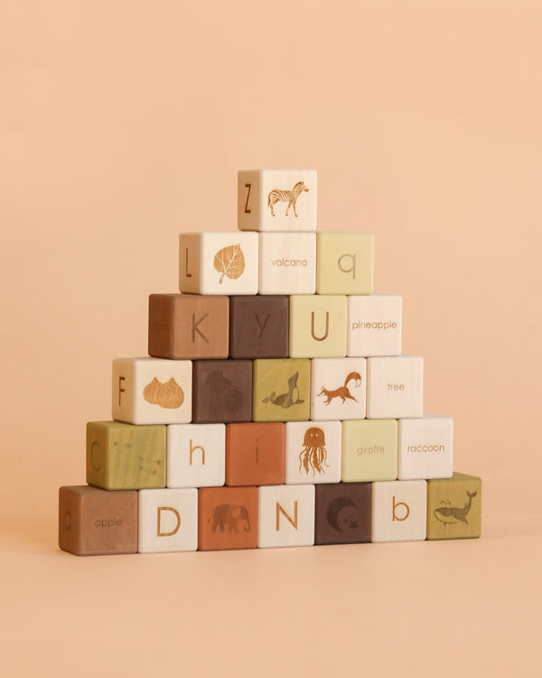 A pyramid of pastel olive-toned alphabet blocks from the Sabo Concept Alphabet Wooden Blocks - Olive set, crafted from natural linden wood and finished with non-toxic paint, is arranged on a beige background. Each block features a letter, an animal name, and an illustration.
