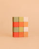 Four rows of three Sabo Concept Mini Wooden Blocks - Flower Meadow, in shades of green, orange, yellow, and white, are neatly stacked against a plain beige background—an engaging educational toy designed to help develop fine motor skills.