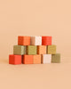 A stack of Sabo Concept Mini Wooden Blocks - Flower Meadow in vibrant shades of orange, green, yellow, pink, and white is arranged in a pyramid shape against a beige background, making it an ideal educational toy for developing fine motor skills.