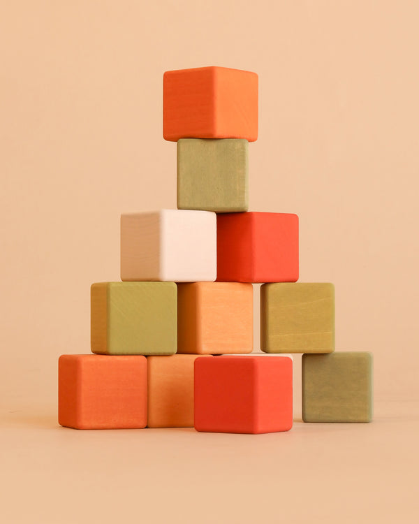 Sabo Concept Mini Wooden Blocks - Flower Meadow features a charming pyramid of colorful wooden blocks in shades of red, orange, green, white, and beige, stacked against a plain tan background. This educational toy encourages the development of fine motor skills while providing vibrant visual appeal.