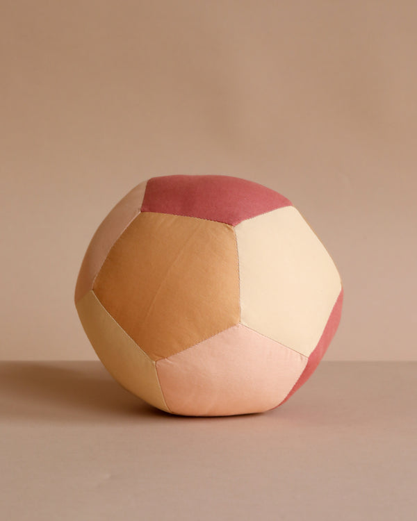 The Fabric Ball - Dusty Rose is a soft, organic cotton baby ball featuring a patchwork design in muted pink, peach, and beige tones, shown on a matching neutral background.