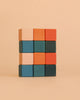 A set of twelve Sabo Concept Mini Wooden Blocks - Tropics, ideal for developing children’s fine motor skills, is arranged in a 4x3 grid. The blocks feature vibrant shades of pink, orange, blue, and dark green, displayed against a plain beige background.