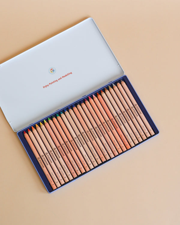 A set of Stockmar Colored Pencils Triangular Assortment 24+1 neatly arranged in a blue tin box, viewed from above. Each pencil is labeled with a light tan body and dark brown text.