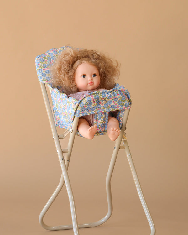 The Konges Sloejd High Chair - Rose Flower features a curly-haired doll in a floral outfit seated in the foldable chair against a plain beige background.