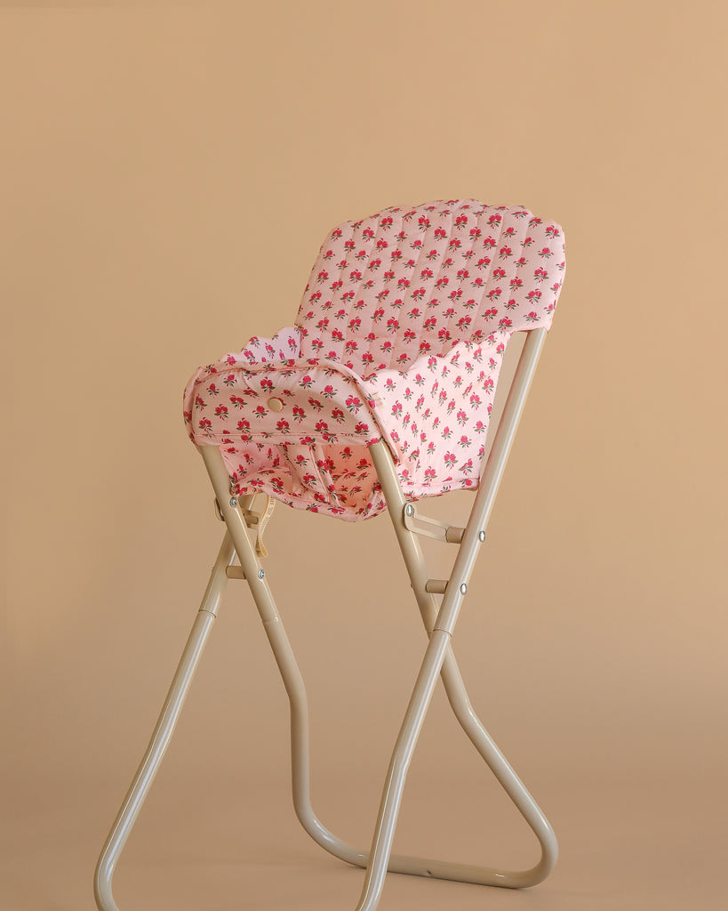 The Konges Sloejd High Chair - Rosie Rose, a beige metal foldable chair with a pink and white floral-patterned cushion and detachable seat, is shown against a plain beige background—perfect for dolls.